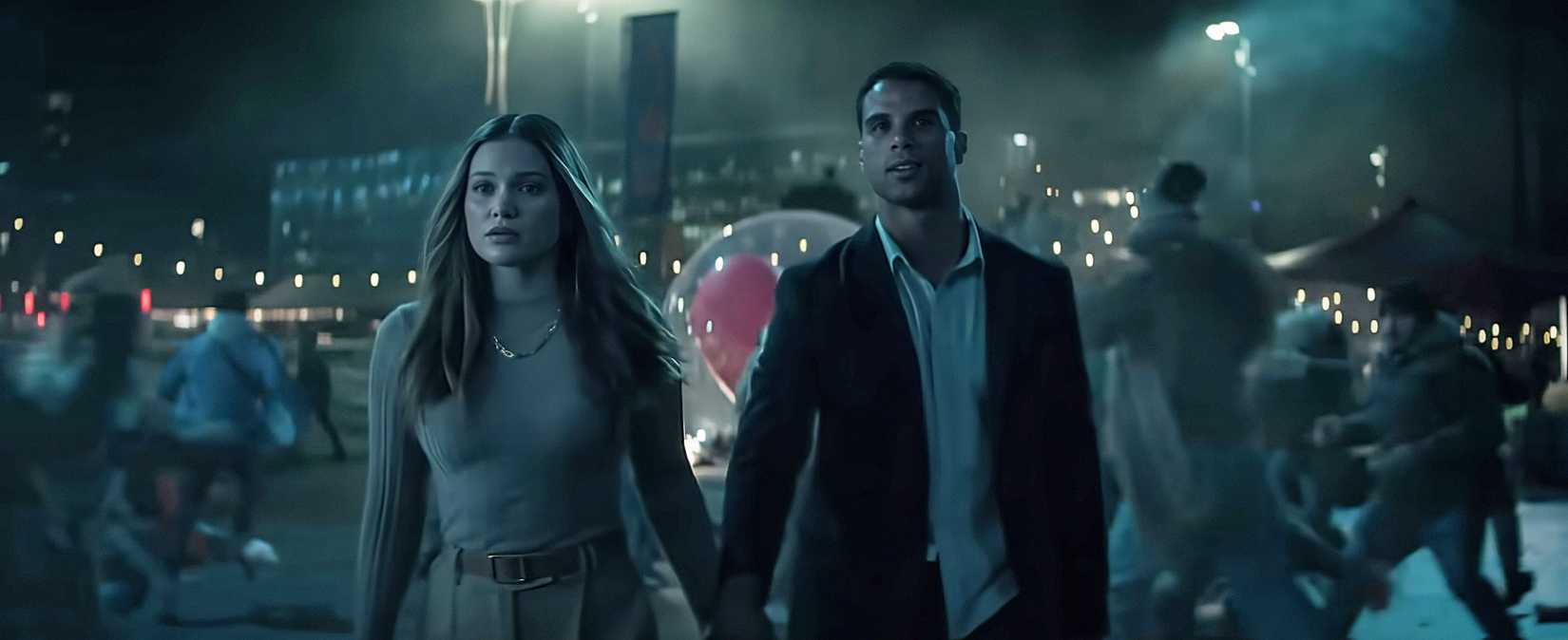 Ally and Jay (Olivia Holt, Mason Gooding), a young couple, hold hands in a public plaza at night, surrounded by strings of lights, in Heart Eyes