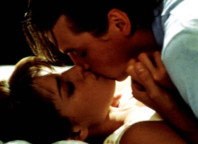 Neve Campbell and Skeet Ulrich in extreme close-up, lying together kissing, with him on top, in the 1996 Scream