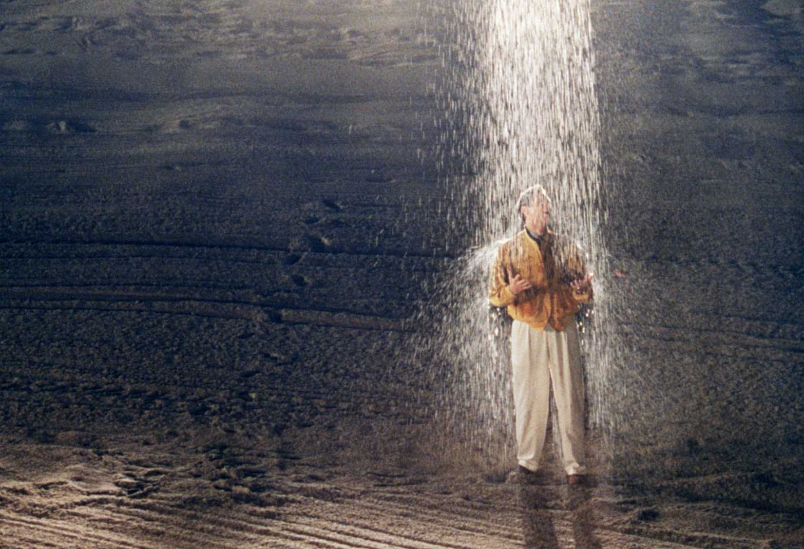 Jim Carrey stands on a beach under a single column of rain in The Truman Show