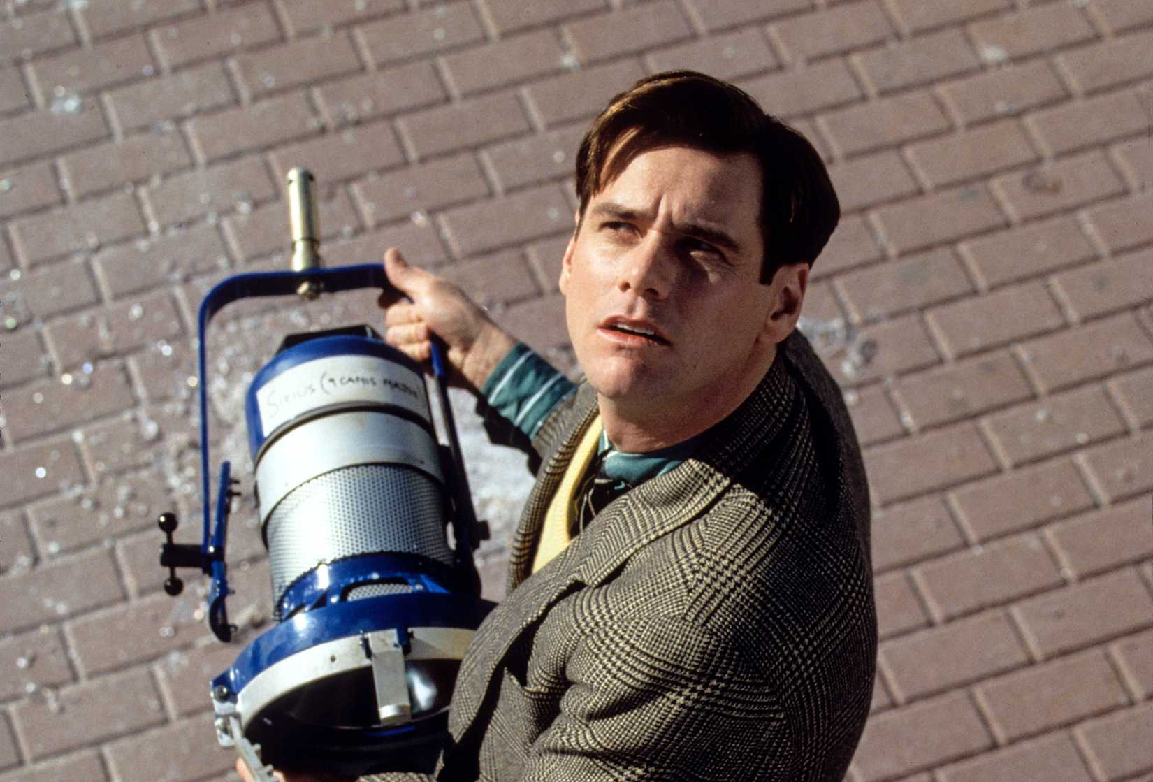 Jim Carrey looks up, confused, while holding a stage light in The Truman Show