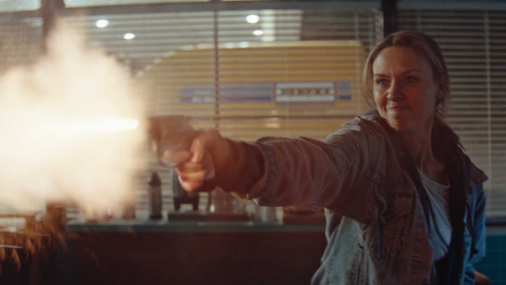 Irene (Michaela McManus) looks fierce as she fires a revolver while standing in a gas station diner in Redux Redux