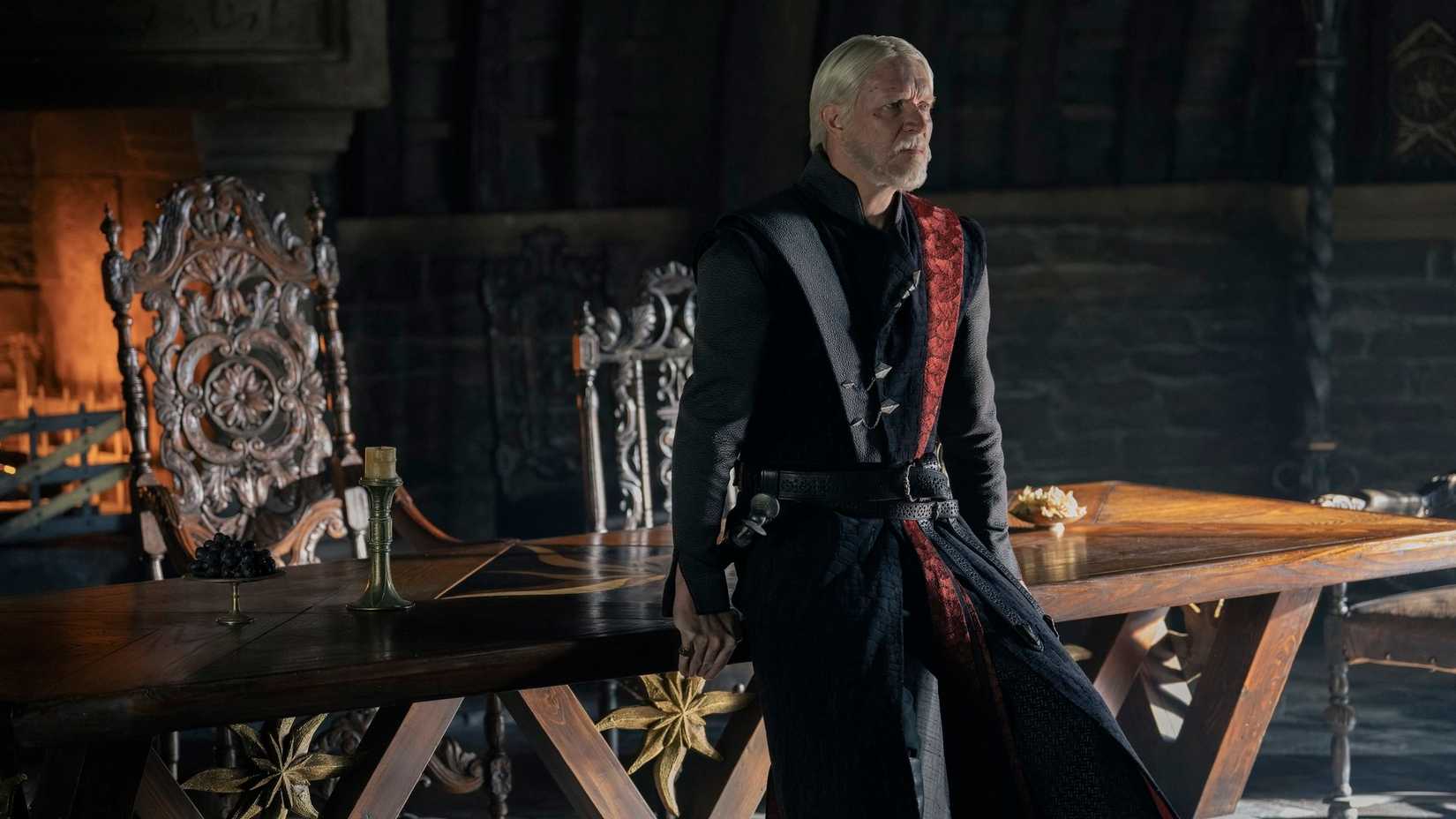 Prince Maekar Targaryen (Sam Spruell), a middle aged man wearing red and black robes, leans on a table looking worried in A Knight of the Seven Kingdoms