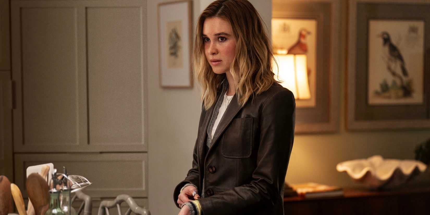 Tatum (Isabel May), the teenage daughter of Sidney (Neve Campbell, not pictured), stands in her home in a medium shot, wearing her mother's old leather jacket, in a scene from Scream 7.