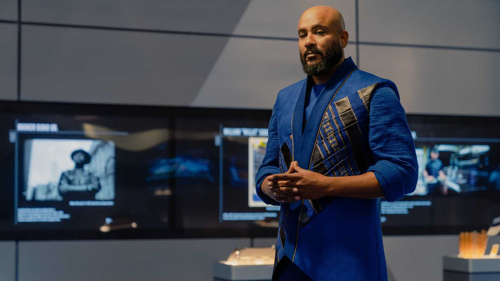 Jake Sisko (Cirroc Lofton), a middle-aged man with a beard in a blue and gold jacket, stands in the Sisko museum in Starfleet Academy looking contemplative