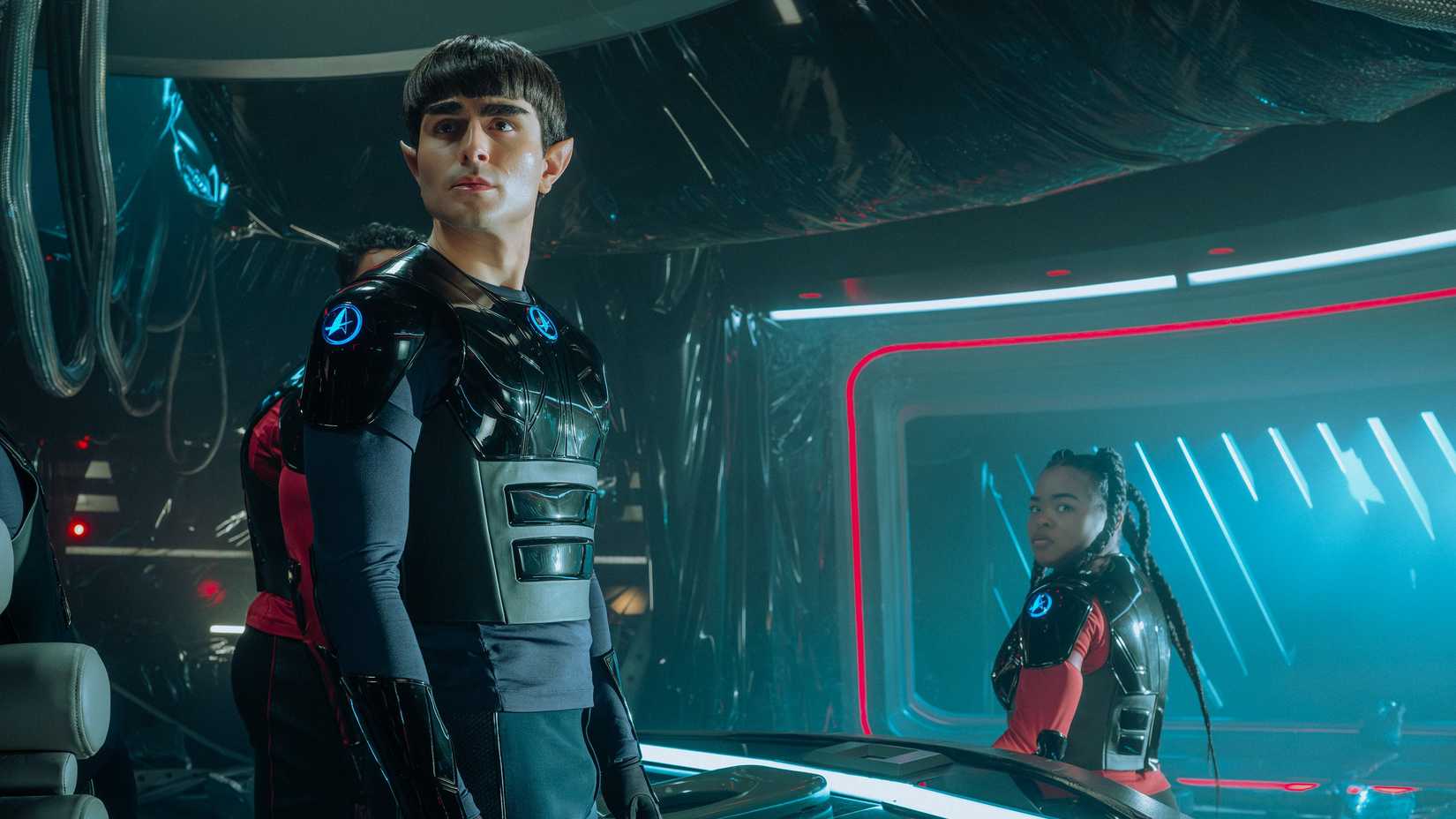 The Vulcan War College student B'Avi (Alexander Eling) and Starfleet Academy cadet SAM (Kerrice Brooks), both wearing armor, stand on the darkened bridge of the USS Miyazaki in Starfleet Academy