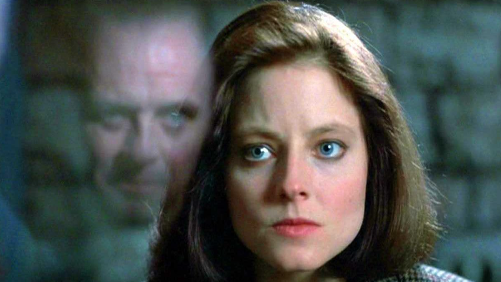 Clarice looks at Hannibal through his glass cell. His face can be seen reflected in the glass.