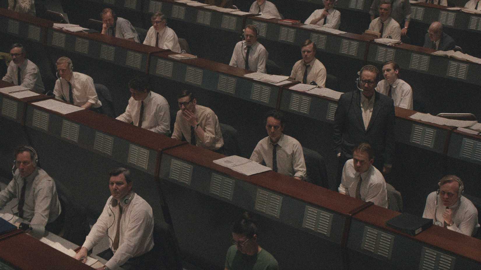 A group of men all wearing white dress shirts and ties and wearing headsets in the Soviet space program command room in Star City