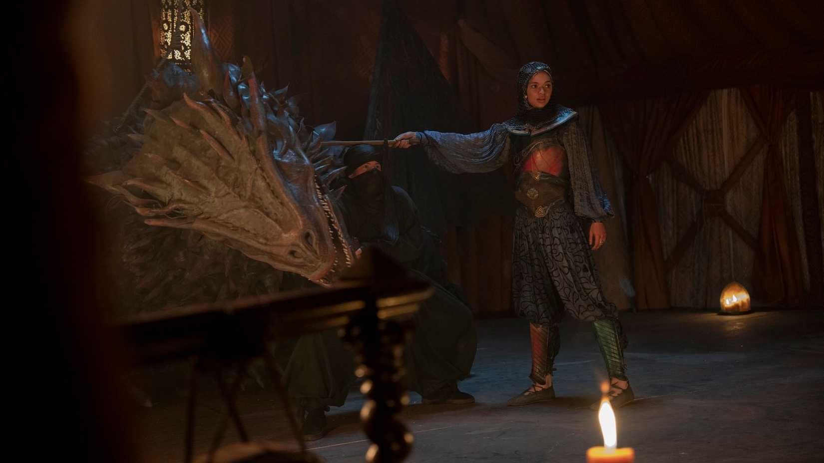 Tanselle (Tanzyn Crawford), a young woman dressed as a knight, holds a sword to the neck of a dragon puppet in A Knight of the Seven Kingdoms