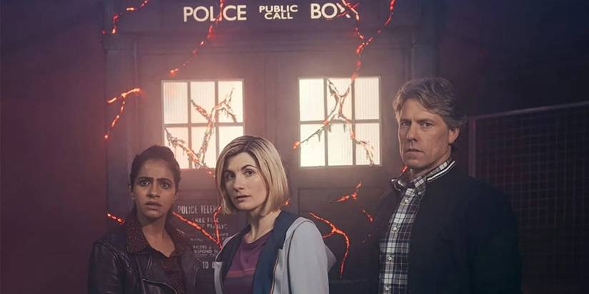 A weathered and cracked TARDIS serves as the backdrop for the cast of Doctor Who.