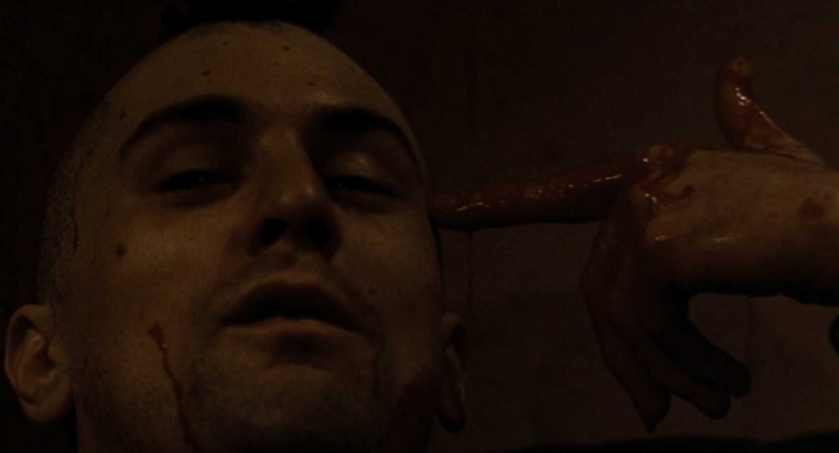 Travis Bickle gestures a mock suicide with a blood-stained hand after a violent confrontation.