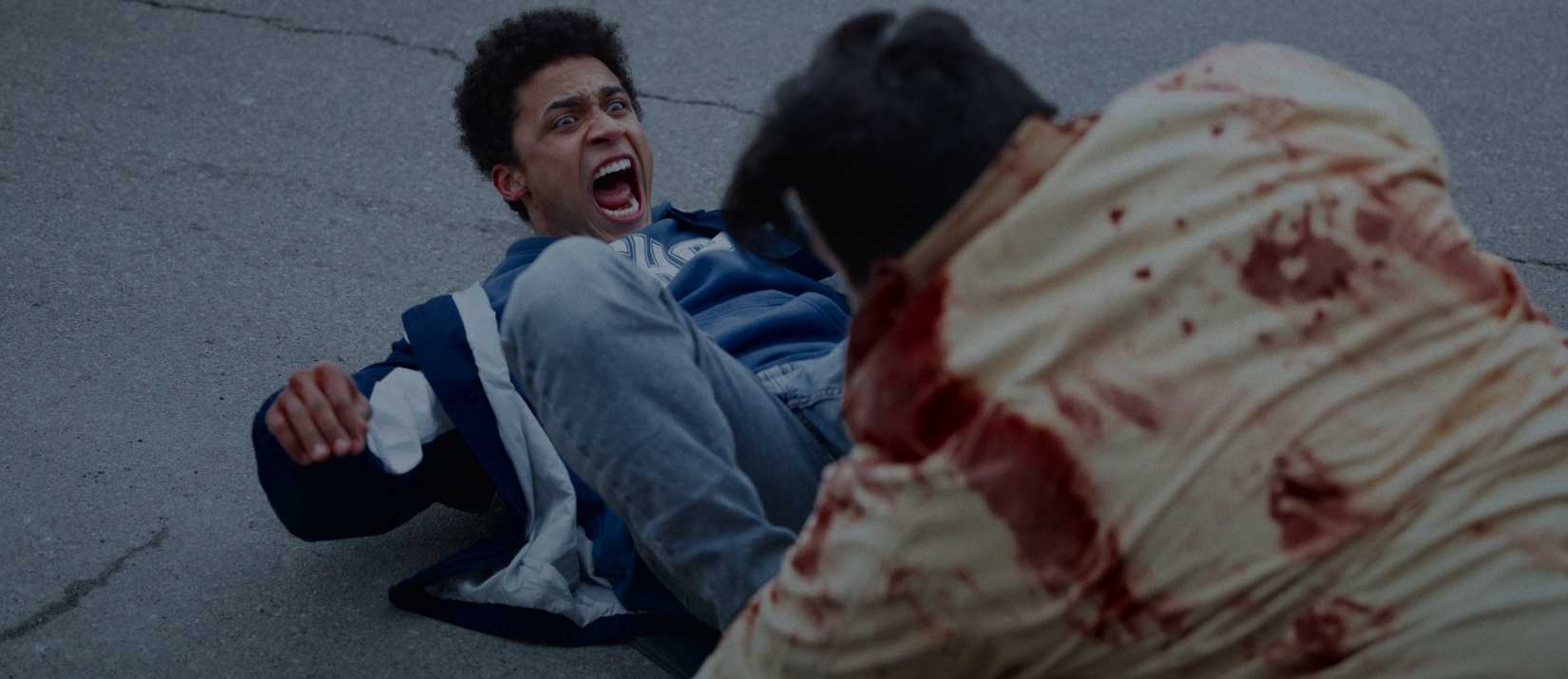 Cary (Corteon Moore) lies on his back in the street, kicking at a blood-covered attacking zombie in This Is Not a Test