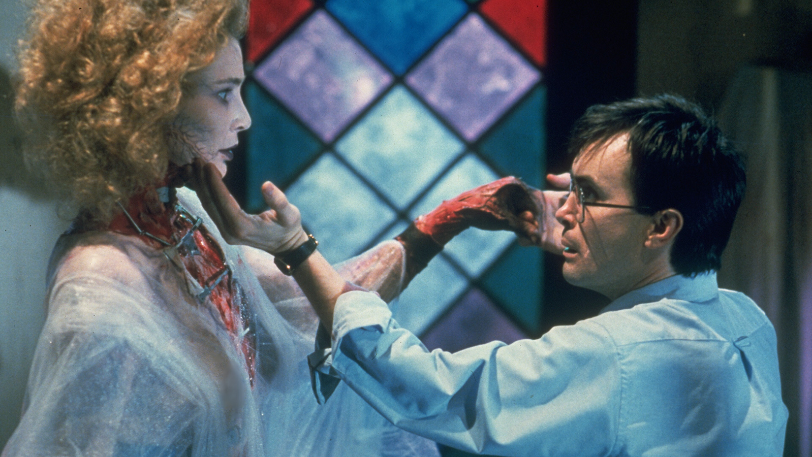 The bespectacled Herbert West gently cups the chin of a re-animated woman (The Bride) in Bride of Re-Animator