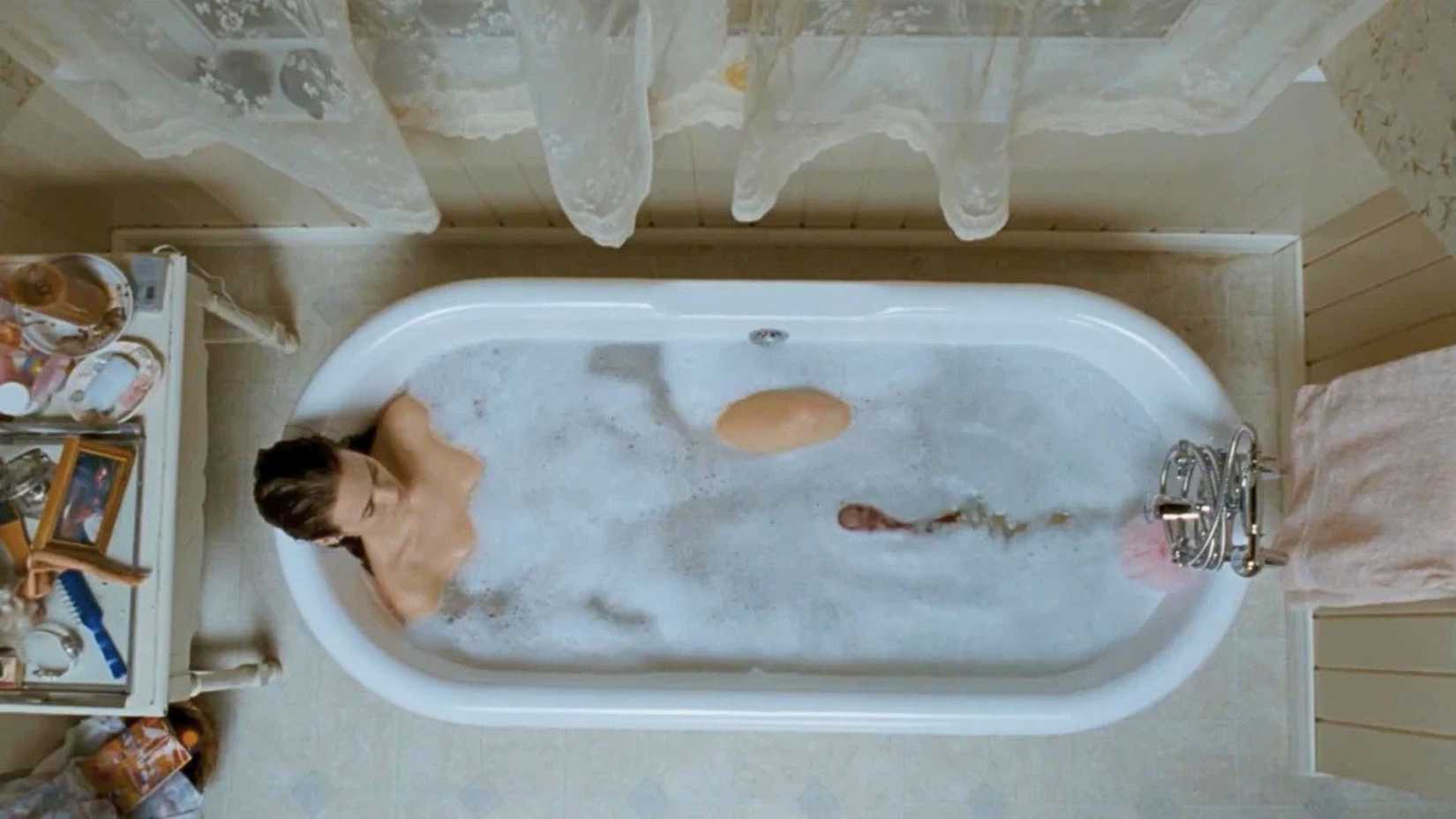 A woman lies in a bath with a slug-like creature roaming through the soap and sudsy water towards her.