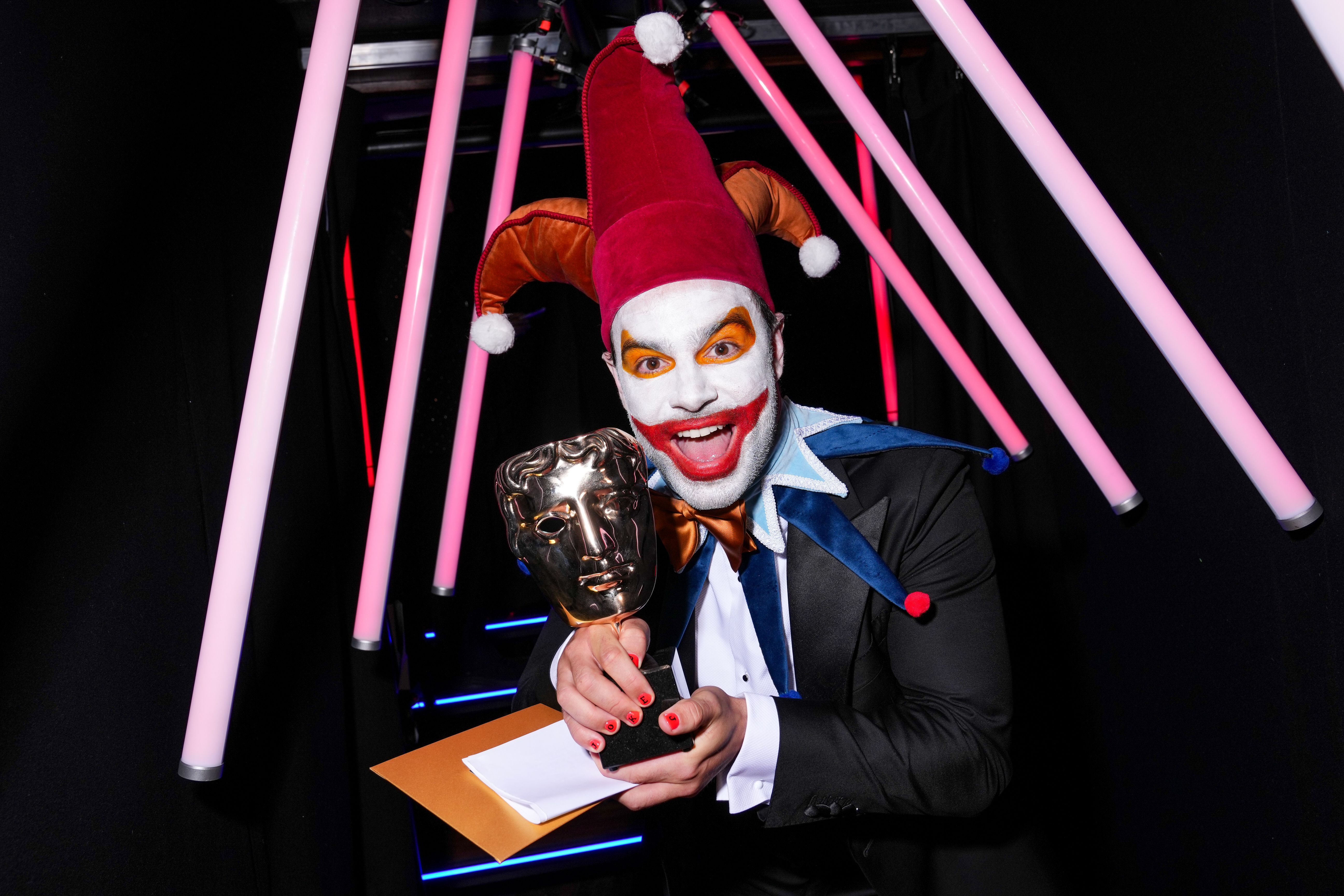 Ben Starr dressed as Balatro's Joker holds an award at the 2025 BAFTA Games Awards