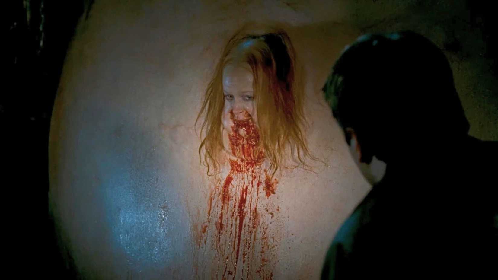 An image featuring a woman who is severey bloated. Her maw is covered in blood, and rank, damp hair covers her face.