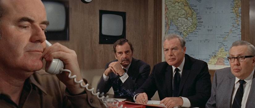 A group of men in suits sit together as one of them attends a call in The Andromeda Strain