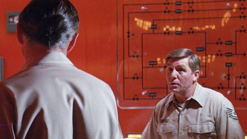A man speaks to his colleague inside a room with blood-red interiors in The Andromeda Strain