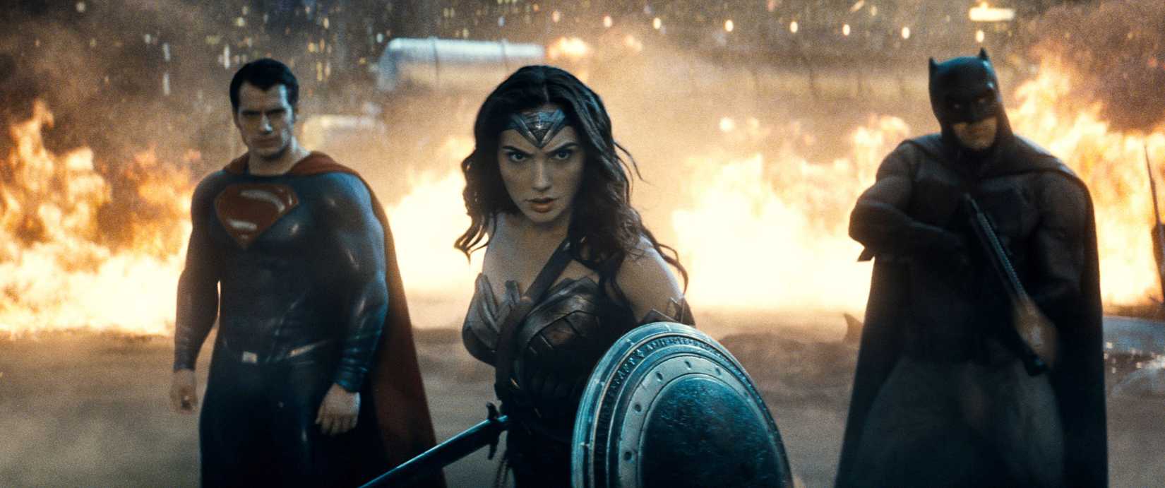 DC's Trinity of Superman, Wonder Woman, and Batman standing ready for battle while a fire rages behind them in an image from Batman v Superman Dawn of Justice.