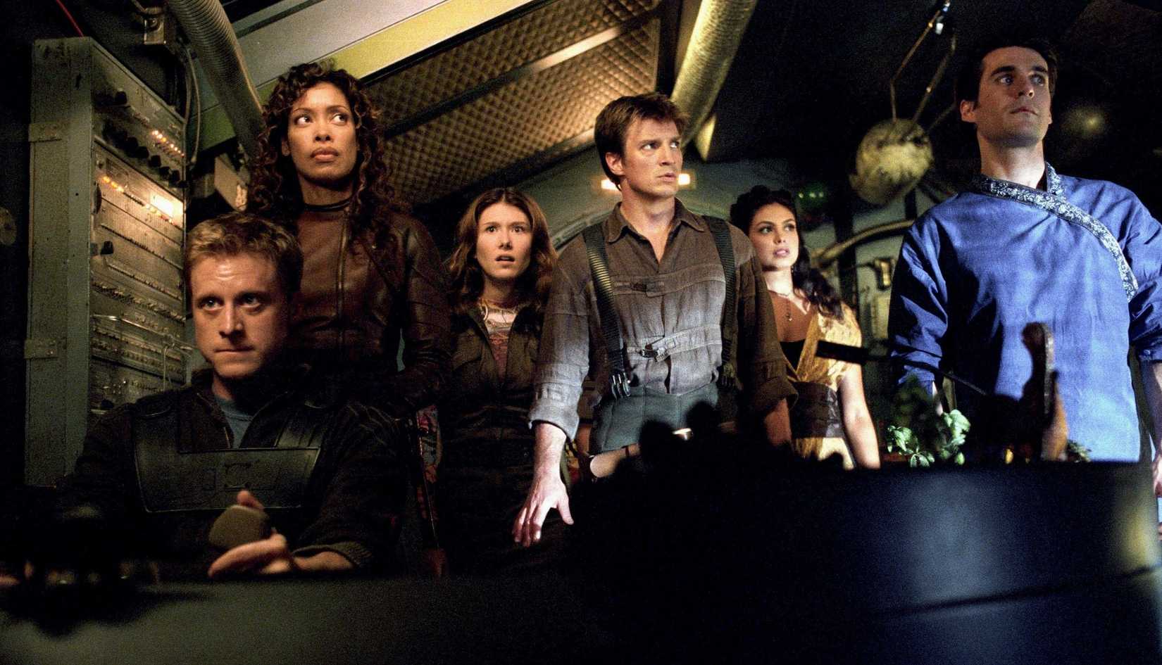 A group shot of cast members of Firefly in costume and in the cockpit of their spaceship in the movie Serenity