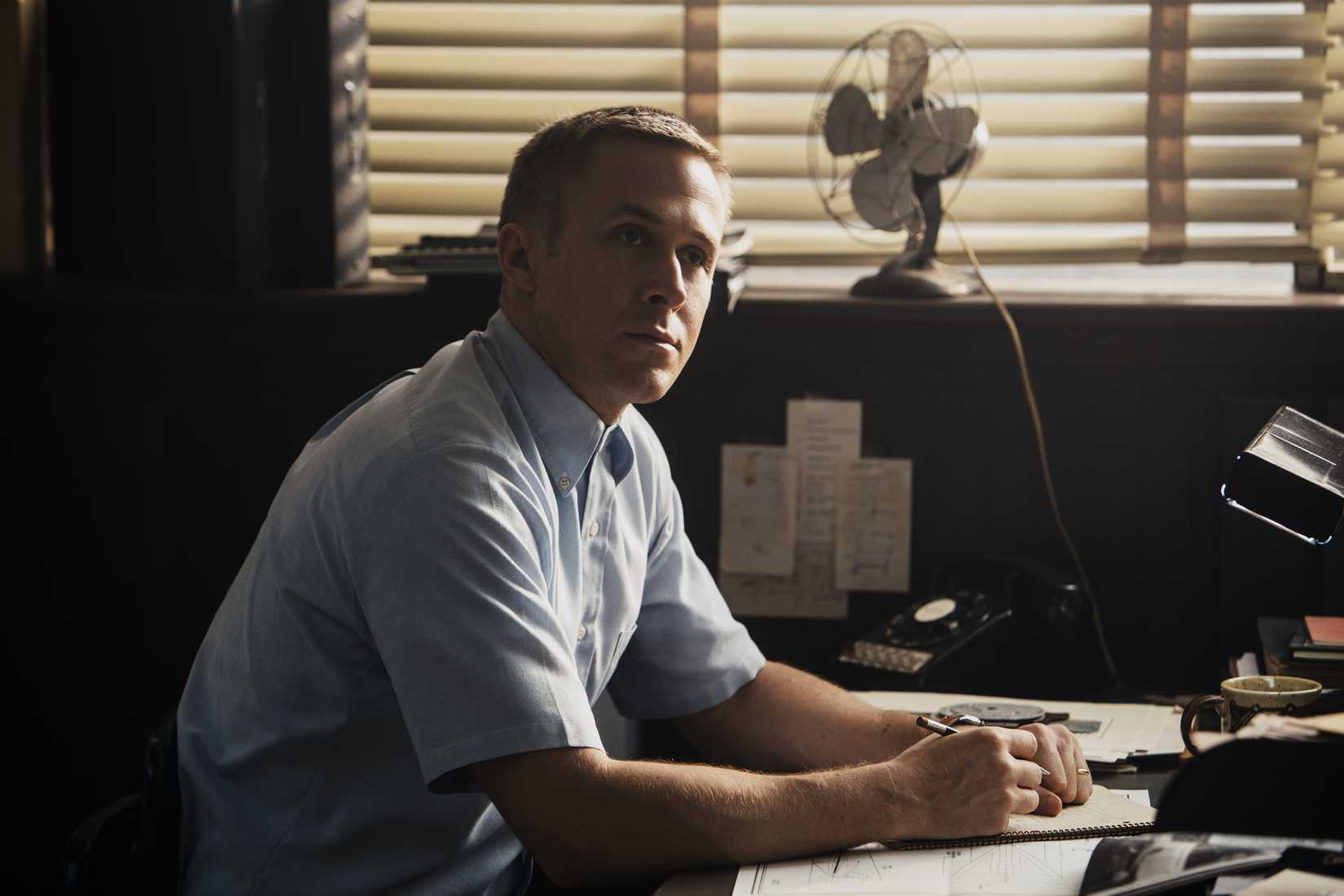 A crew-cut, serious-looking Neil Armstrong (Ryan Gosling) mans a desk in a scene from First Man (2018). 