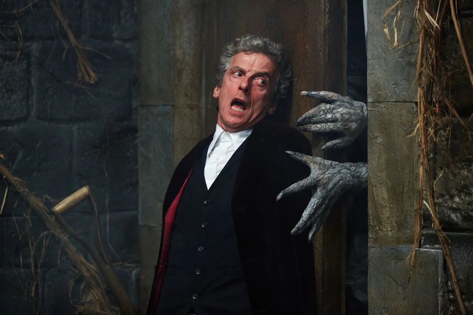 The 12th Doctor tries to press a door closed while monster hands reach for him