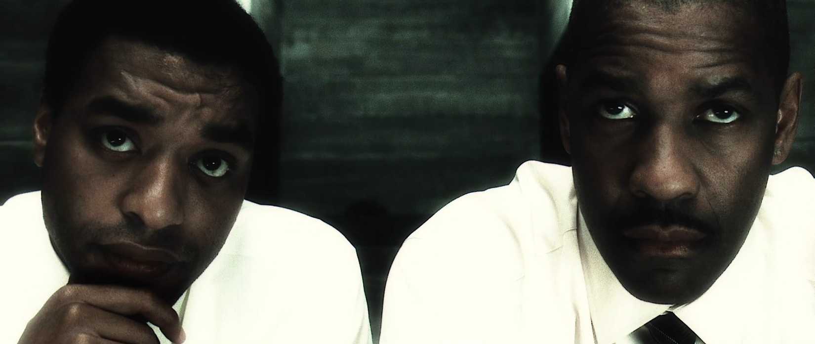 Denzel Washington and Chiwetel Ejiofor sit side-by-side in close-up in a scene from Inside Man that uses a high-contrast, bleachy effect on the film stock to make their white jackets especially bright.  