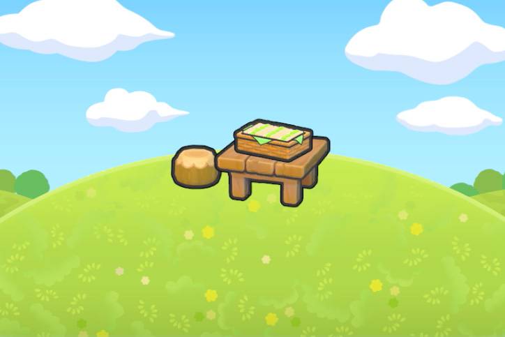 A picnic basket full of sandwiches sitting on top of a wooden table beside a stool on a grassy hill in Pokémon Pokopia.