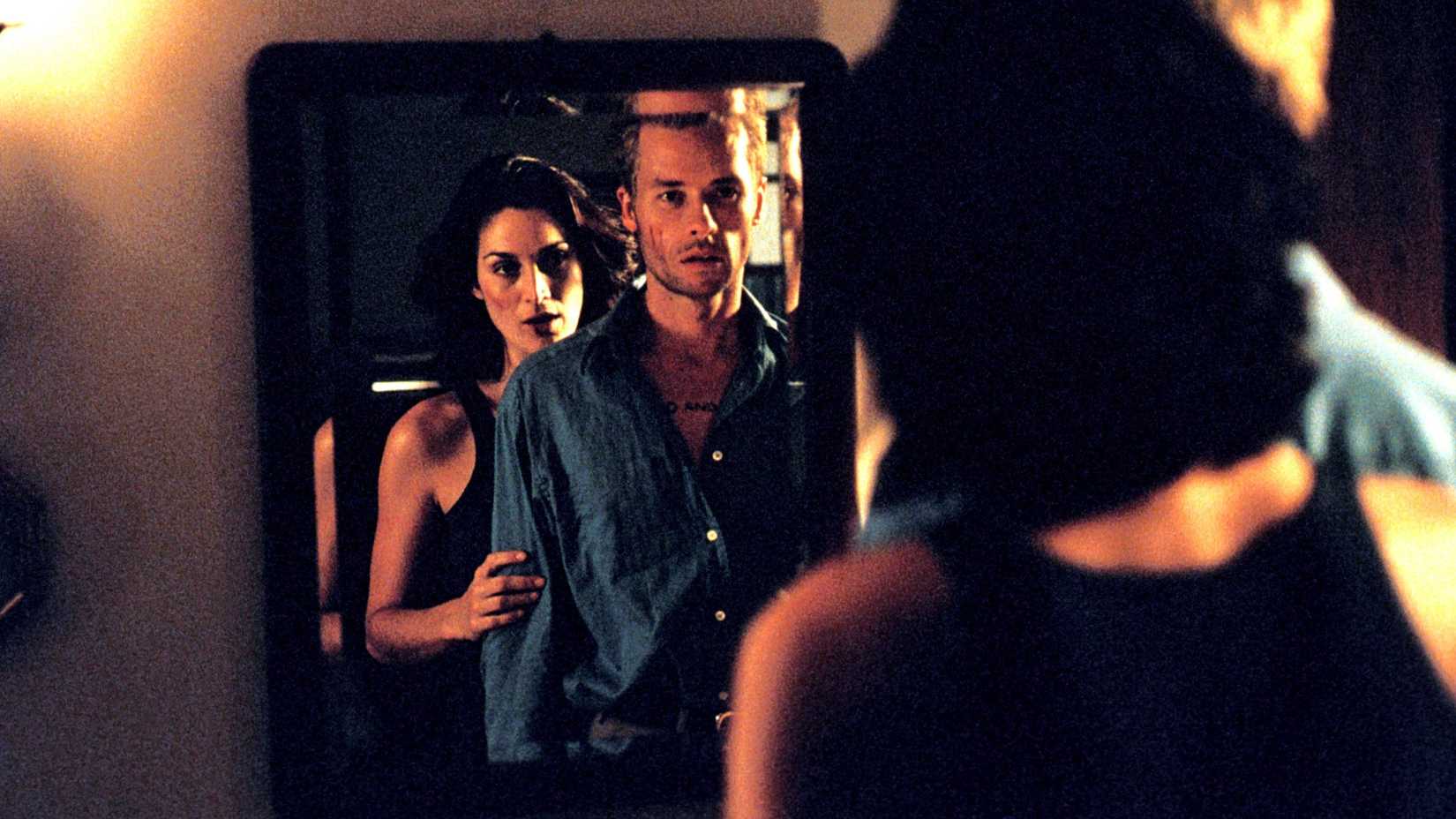 Natalie (Carrie-Anne Moss) stands behind Leonard (Guy Pearce) in front of a mirror in Memento