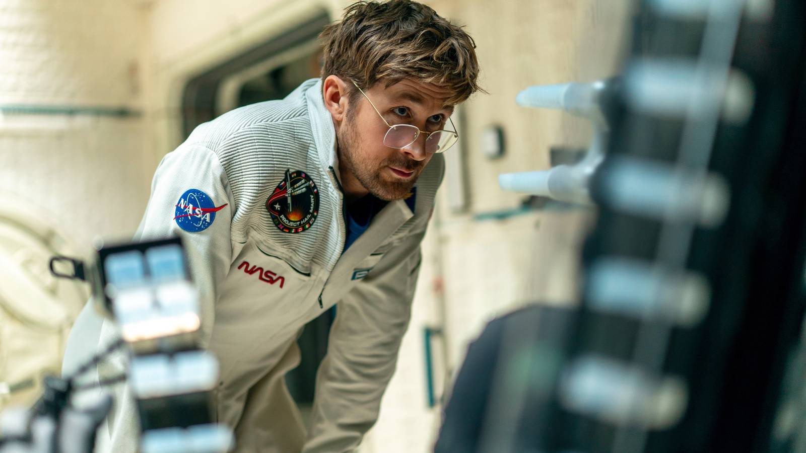 Project Hail Mary — Ryan Gosling wears a white NASA jumpsuit and stares intensely at something offscreen