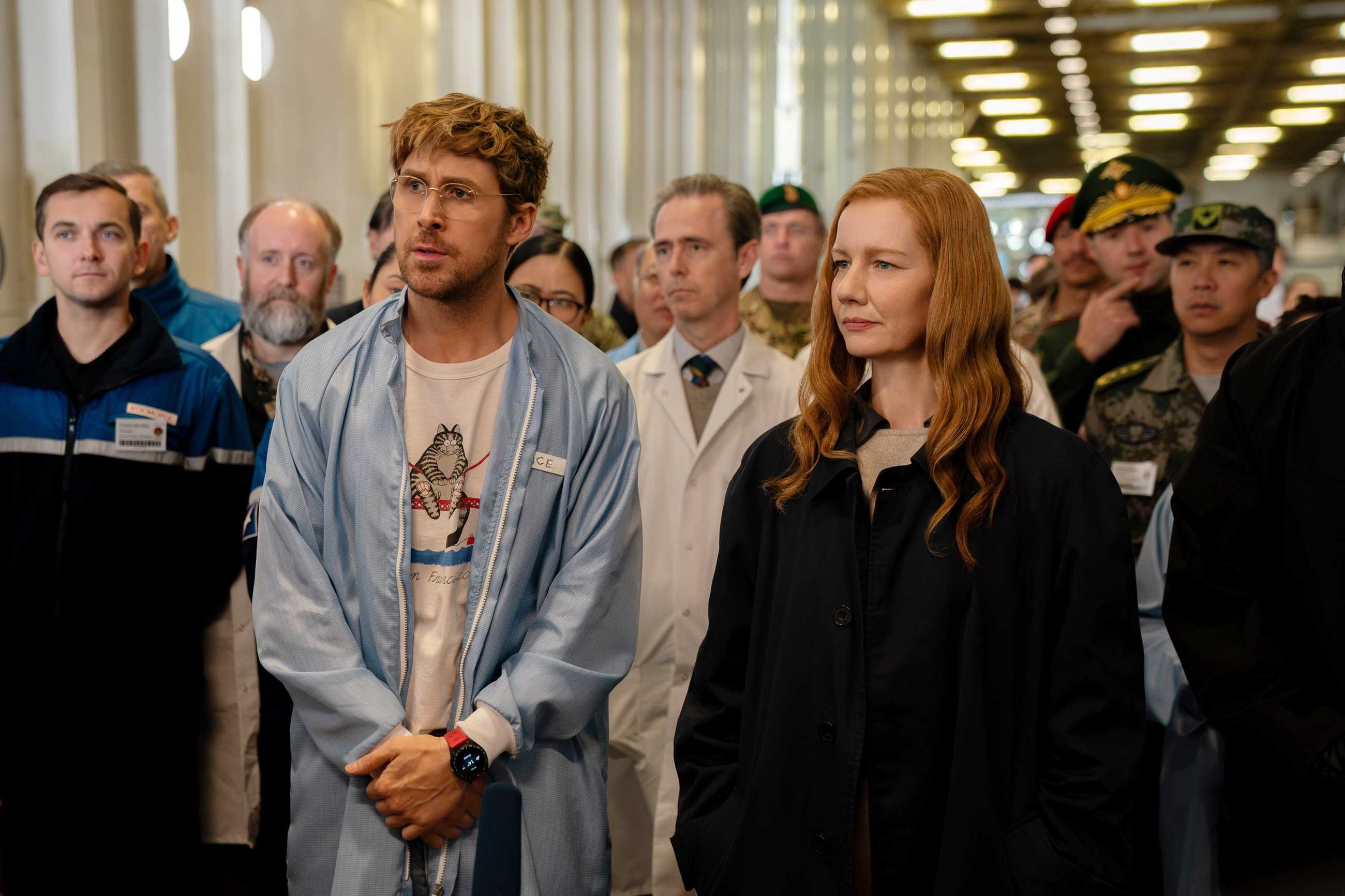 Ryland Grace (Ryan Gosling) and Eva Stratt (Sandra Hüller) lead a crowd through a narrow facility corridor