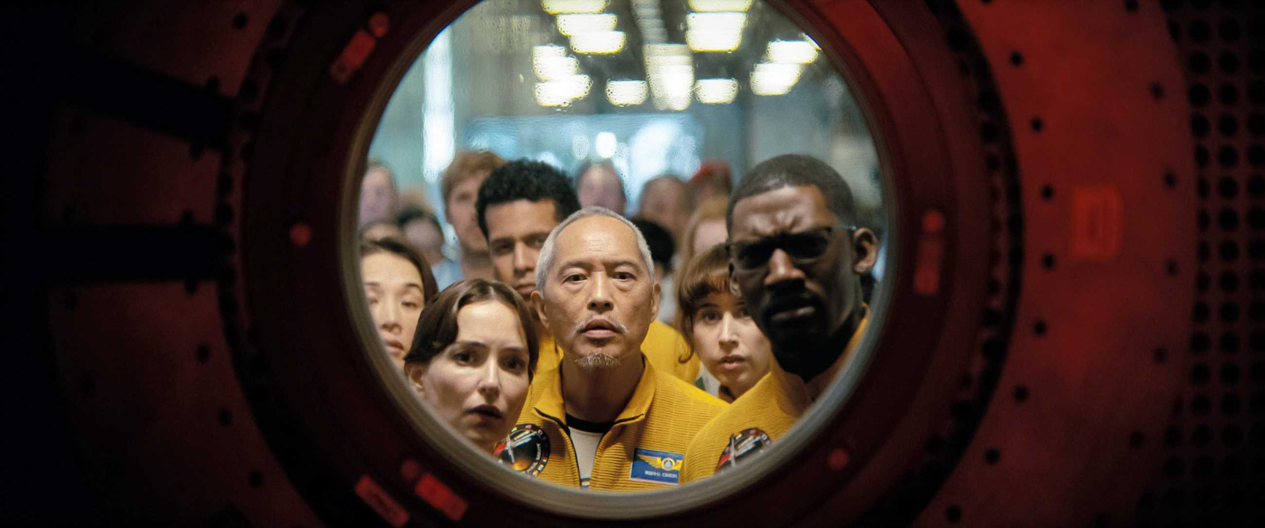 A group of people in yellow suits peering through a round window into a dark space