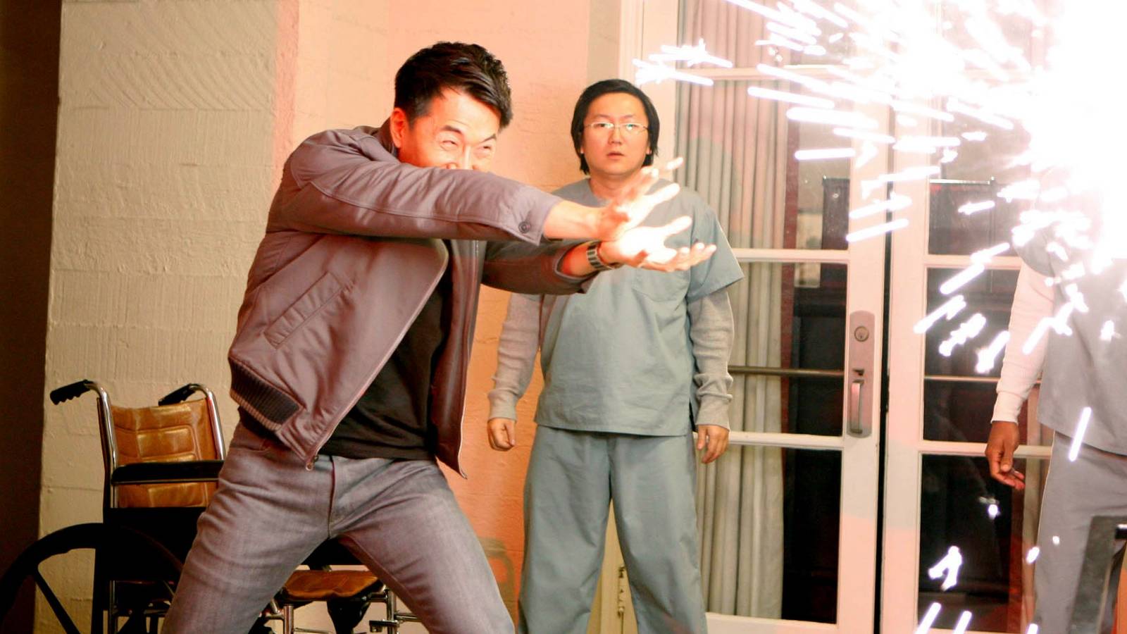 James Kyson Lee blasts a wall with an explosion of sparks as Masi Oka stands by in Heroes