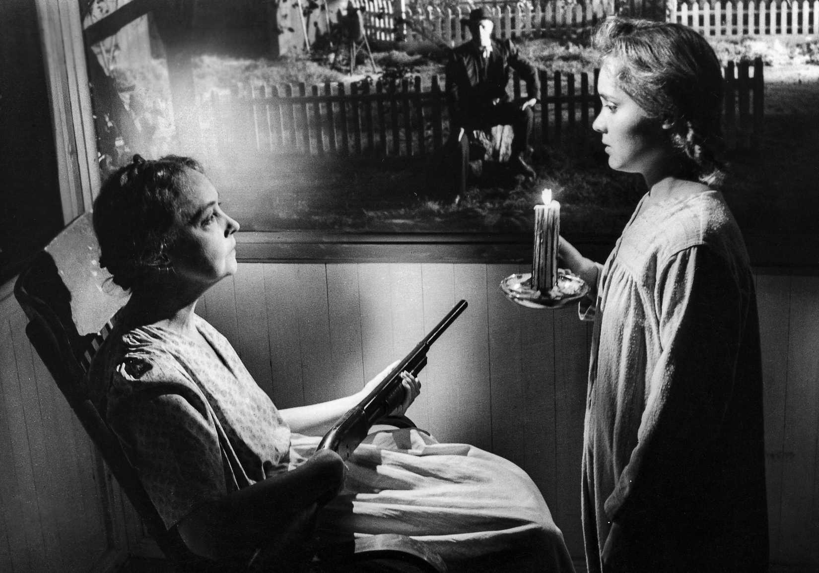 Lillian Gish sits in a rocking chari with a shotgun talking to a young girl. Through her screen window you can see Robert Mitchum sitting on a tree stump