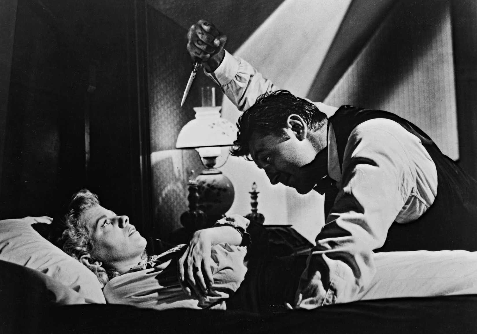 Robert Mitchum raises a knife over Shelley Winters lying in bed in The Night of the Hunter