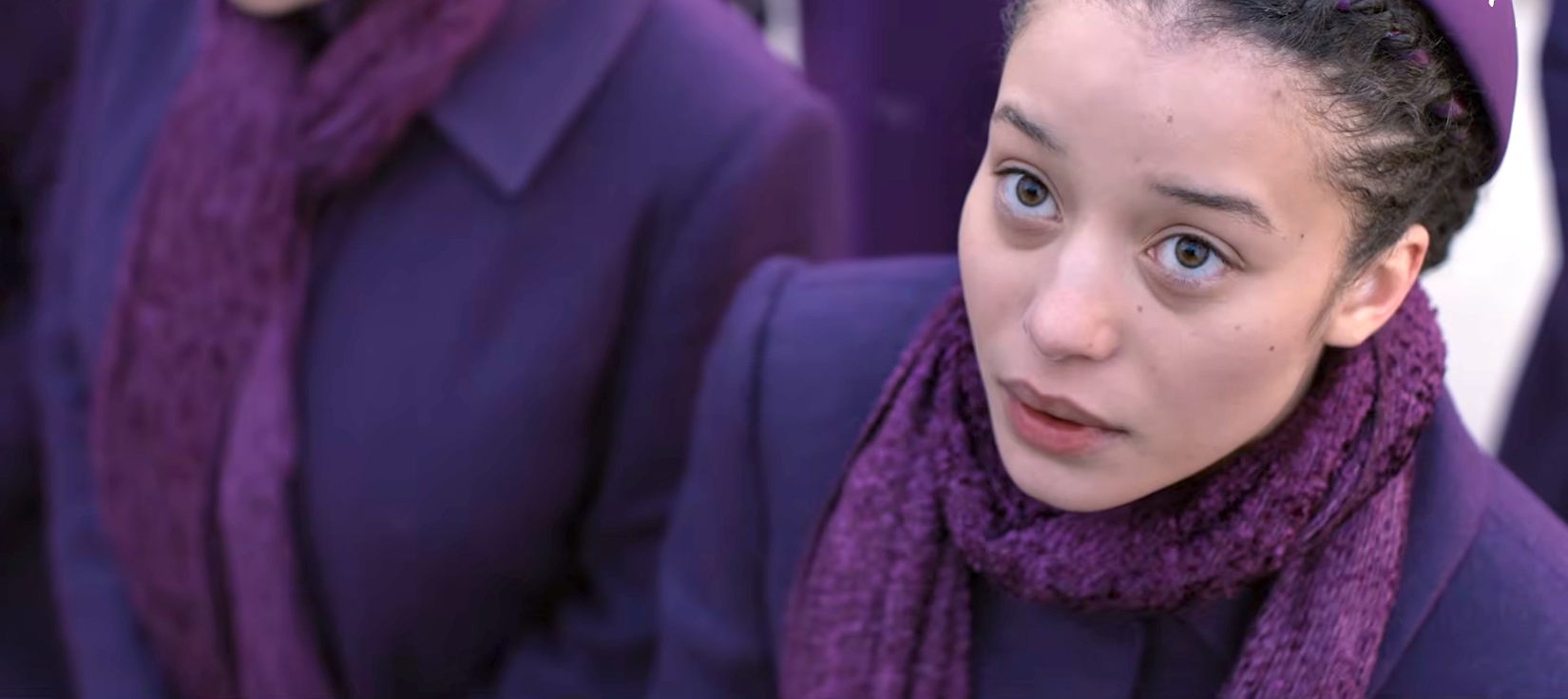 An image of a young woman in purple looking upward, from The Testaments