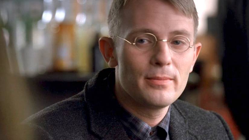A young man wearing a suit and rounded glasses sits in a diner in the Fringe episode The Bishop Revival