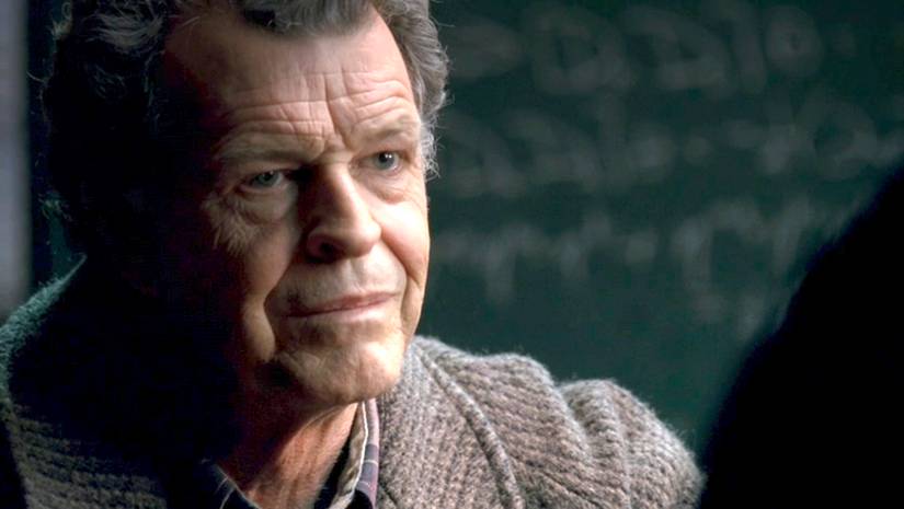 Walter Bishop (John Noble) wearing a sweater stands in front of a chalkboard covered with equations in the Fringe episode "White Tulip"