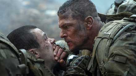 Army sergeant 81 (Alan Ritchson) leans over a fellow solder and covers their mouth with his hand to keep them quiet in War Machine