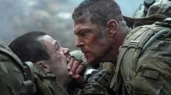 Army sergeant 81 (Alan Ritchson) leans over a fellow solder and covers their mouth with his hand to keep them quiet in War Machine