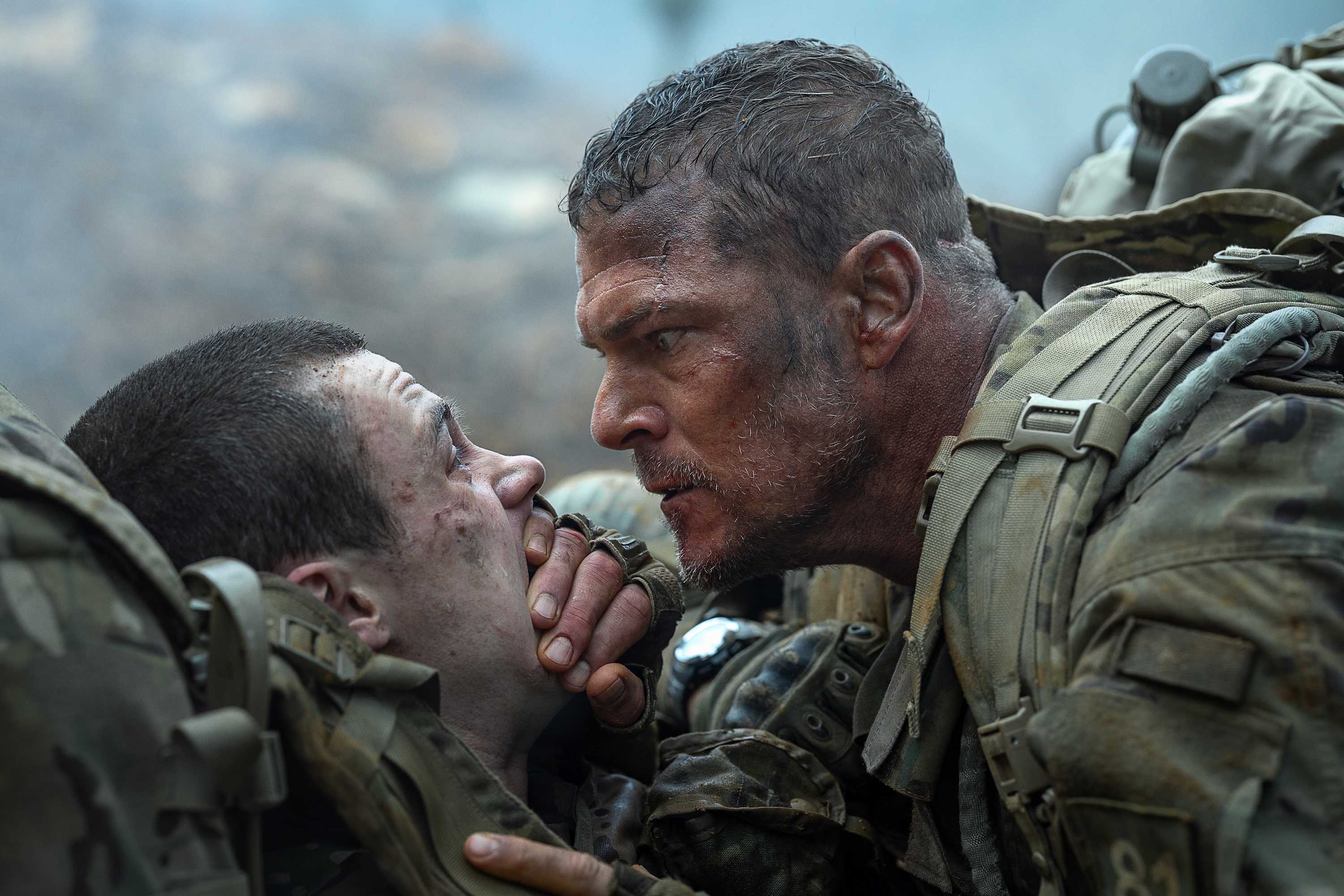 Army sergeant 81 (Alan Ritchson) leans over a fellow solder and covers their mouth with his hand to keep them quiet in War Machine