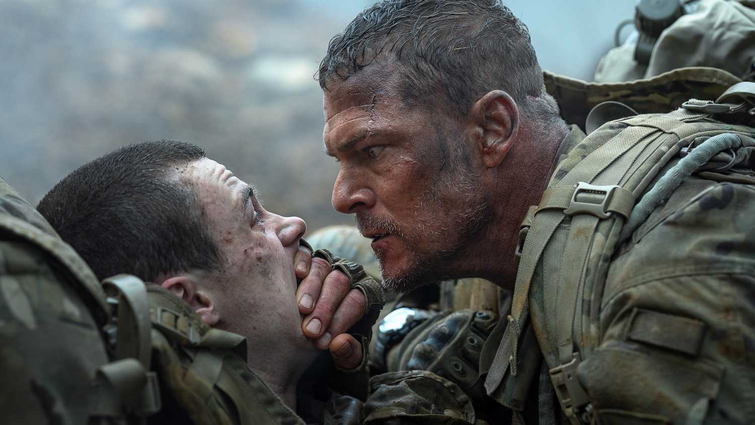 Army sergeant 81 (Alan Ritchson) leans over a fellow solder and covers their mouth with his hand to keep them quiet in War Machine