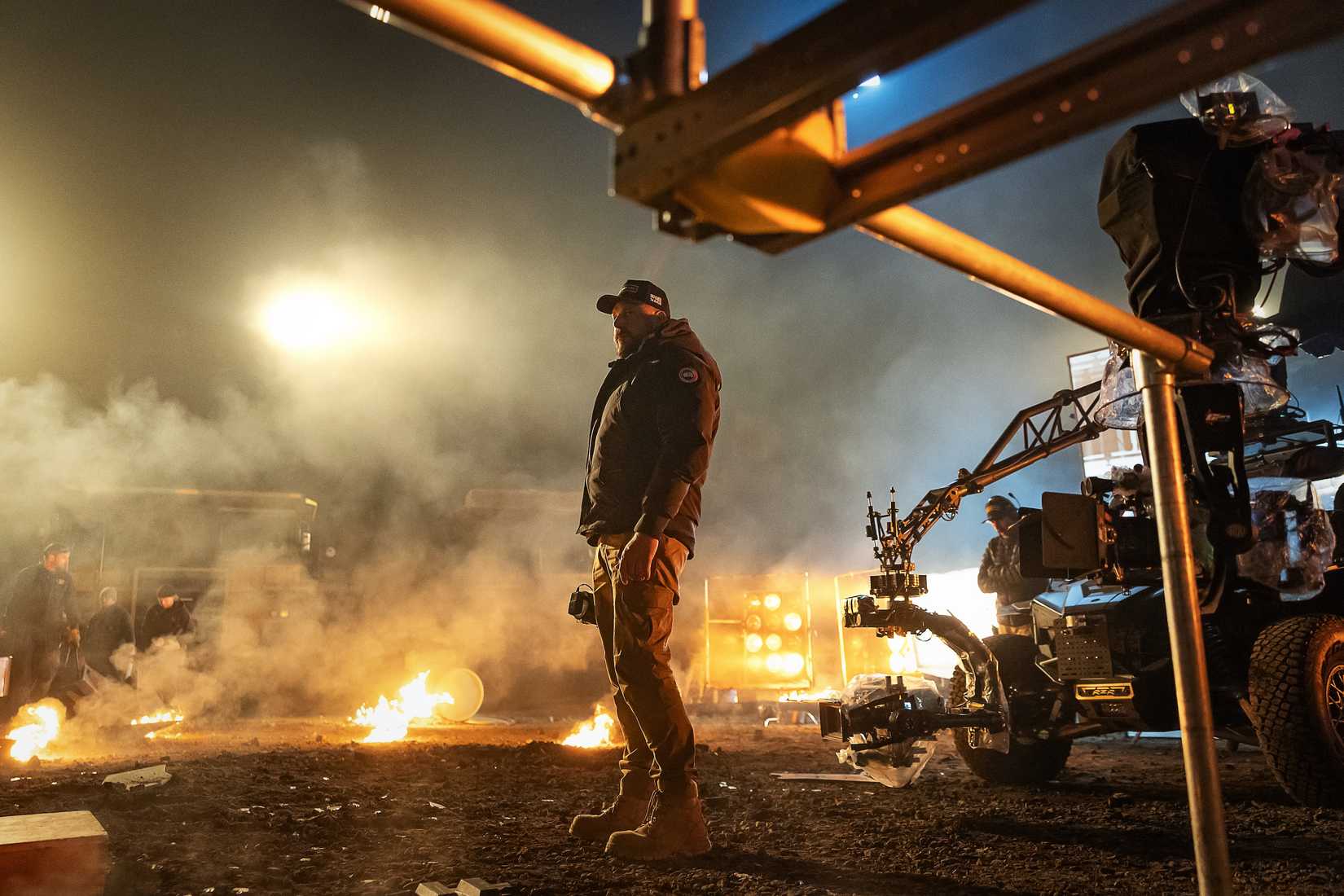 Director Patrick Hughes during the production of War Machine, standing in a nighttime field surrounded by fire and camera equipment