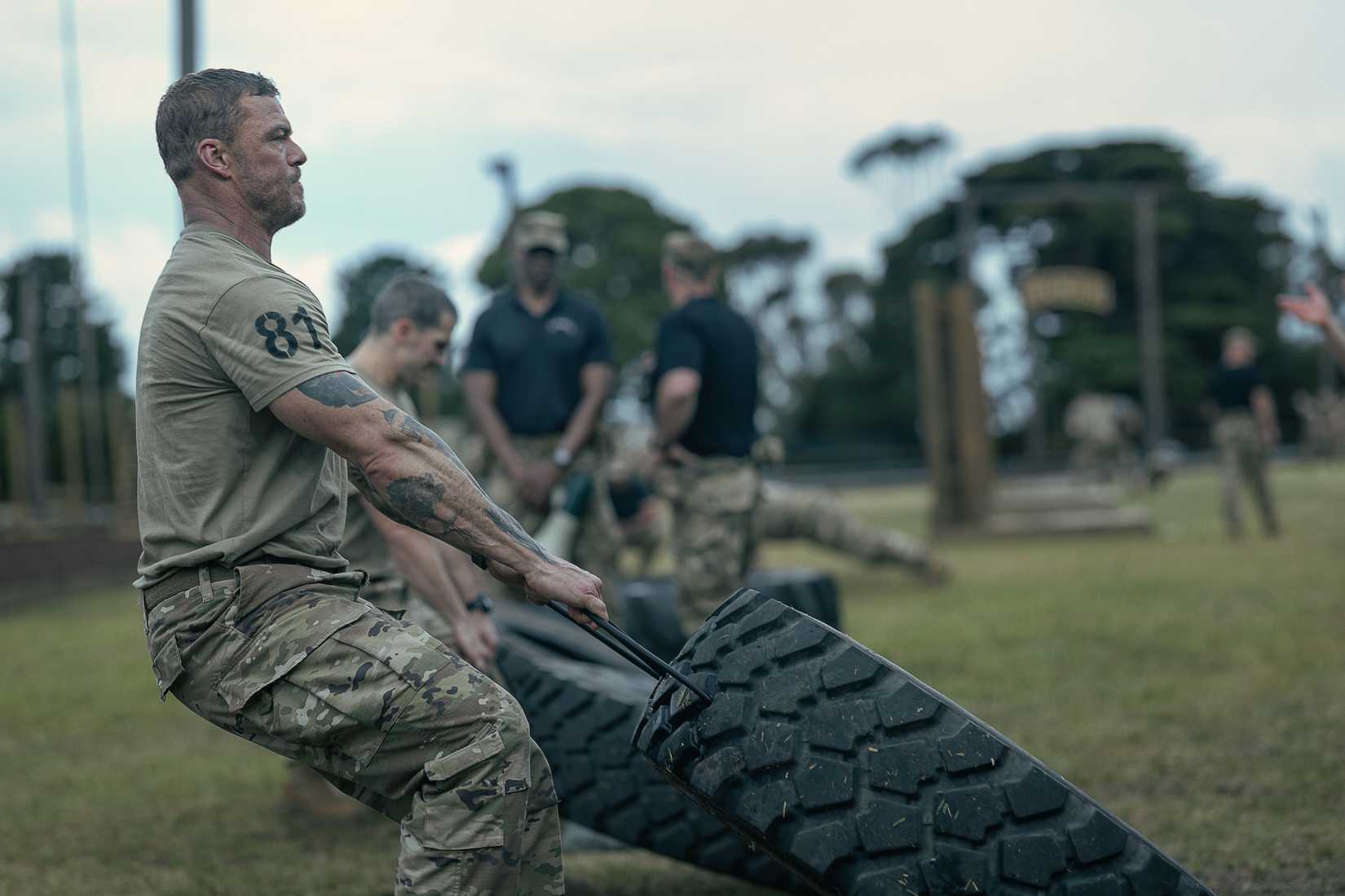 81 (Alan Ritchson), an Army sergeant in camo pants and a T-shirt, clenches his jaw as he drags a huge tire alongside a line of other Ranger candidates doing the same in War Machine