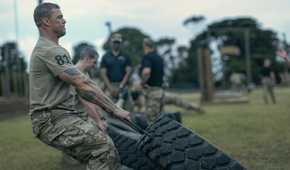 81 (Alan Ritchson), an Army sergeant in camo pants and a T-shirt, clenches his jaw as he drags a huge tire alongside a line of other Ranger candidates doing the same in War Machine