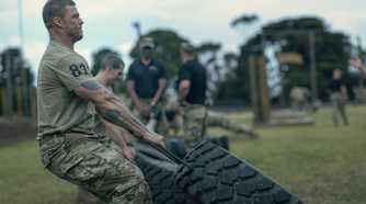 81 (Alan Ritchson), an Army sergeant in camo pants and a T-shirt, clenches his jaw as he drags a huge tire alongside a line of other Ranger candidates doing the same in War Machine