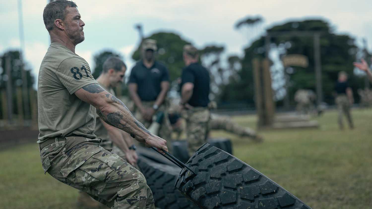 81 (Alan Ritchson), an Army sergeant in camo pants and a T-shirt, clenches his jaw as he drags a huge tire alongside a line of other Ranger candidates doing the same in War Machine