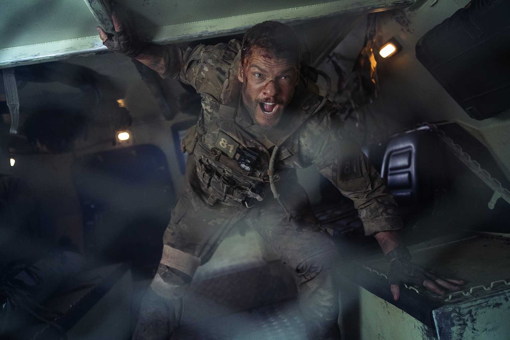 Army sergeant 81 (Alan Ritchson) stands in the back of an armored transport and yells through a metal grate in War Machine