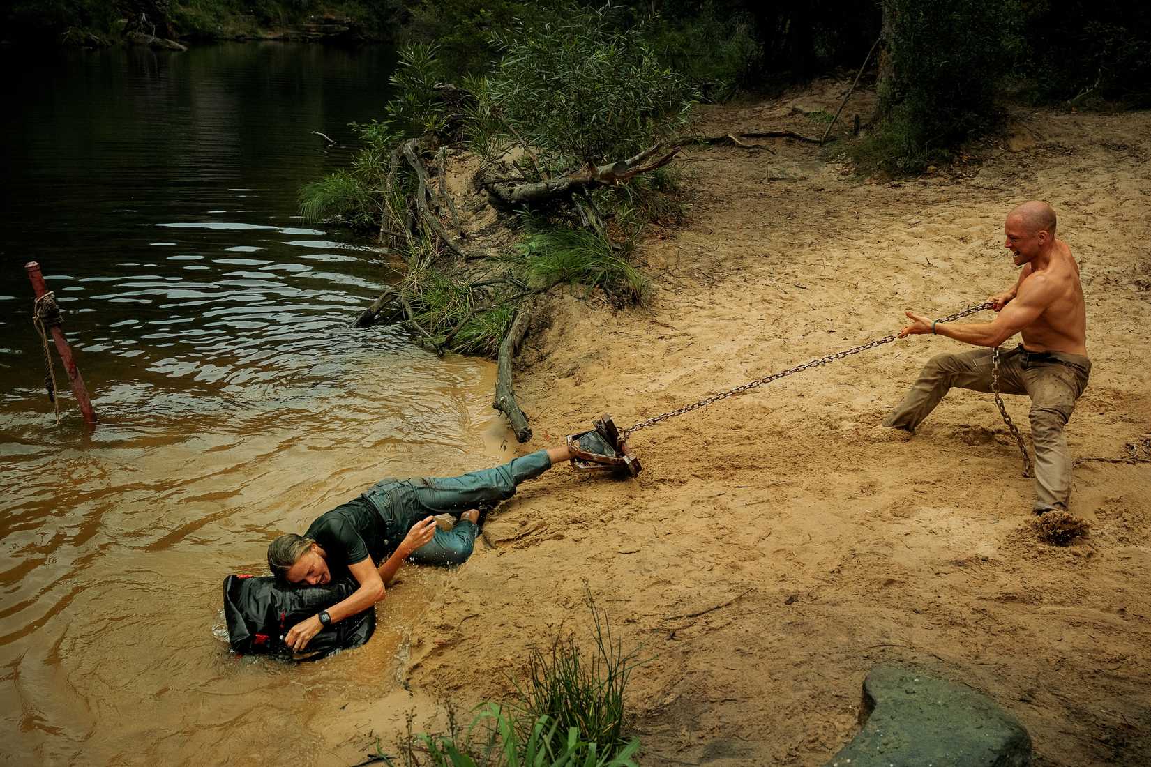 Taron Egerton hauls Charlize Theron across a sandy beach by a chain attached to a bear trap on her leg in Apex
