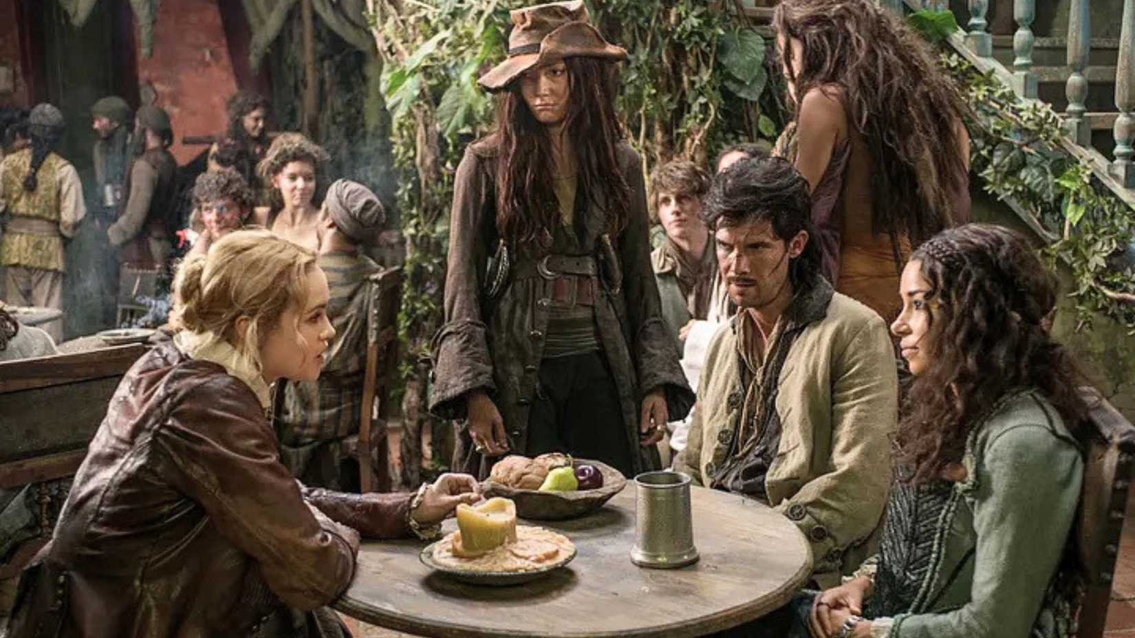 An image featuring Hannah New as Eleanor Guthrie and Jessica Parker Kennedy as Max. They are joined by Clara Paget as Anne Bonny and Toby Schmitz as Jack Rackham. Together, all four sit a table, looking tense and terse.