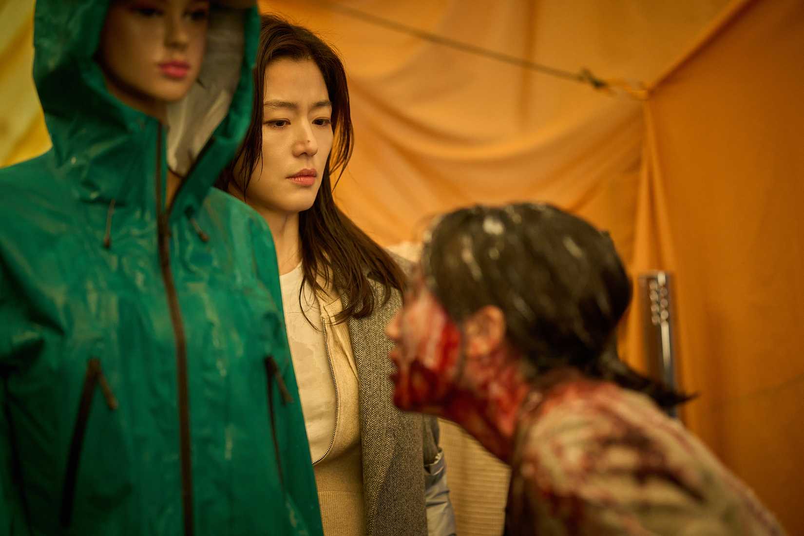 A frightened-looking Korean woman tries to keep emotion off her face while a blood-covered humanoid sniffs at her in Colony